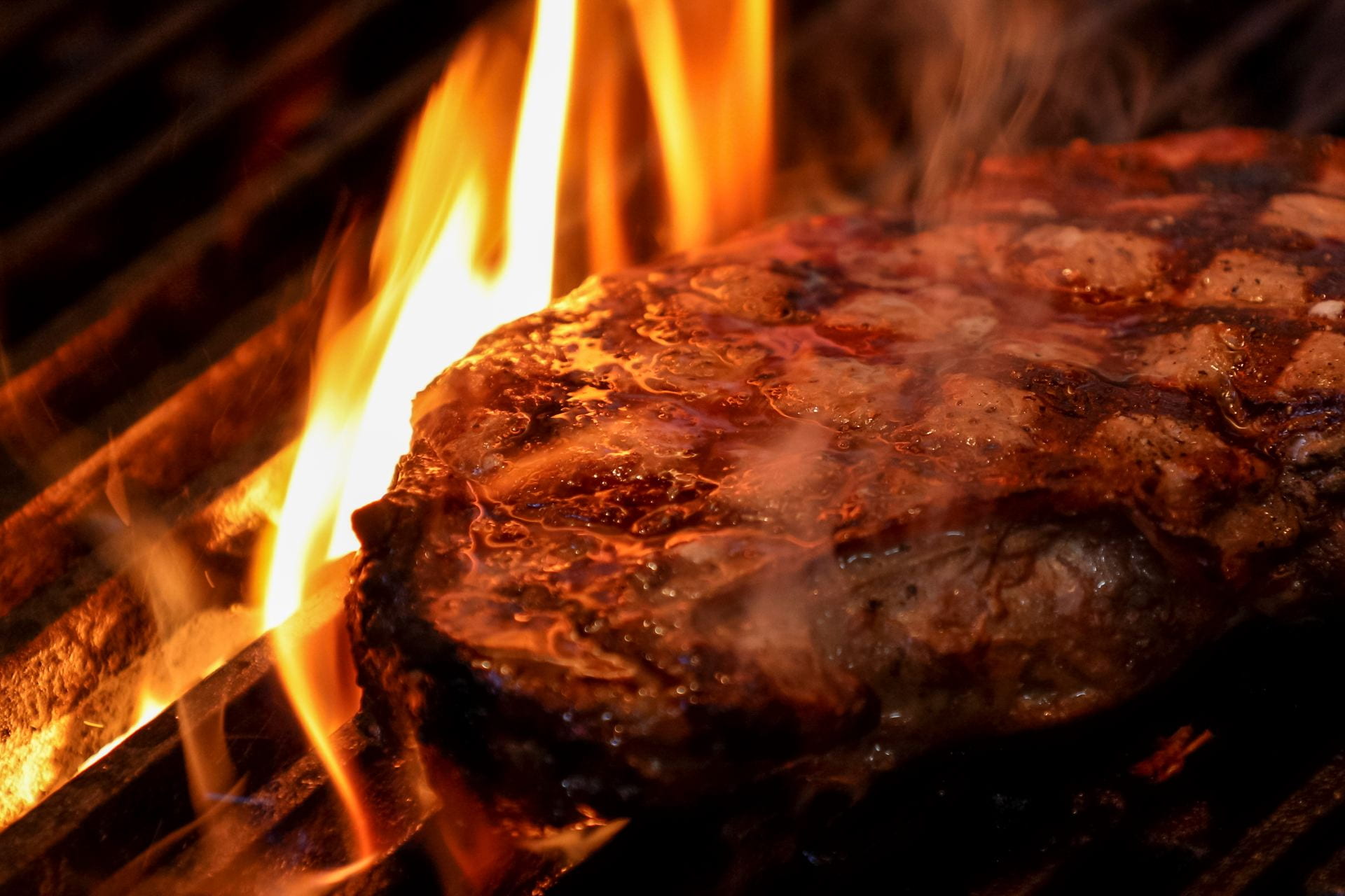 Close up of a steak on a grill with flames beneath.