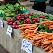 Table at a farmers market, displaying lettuce, asparagus, radishes and carrots for sale.