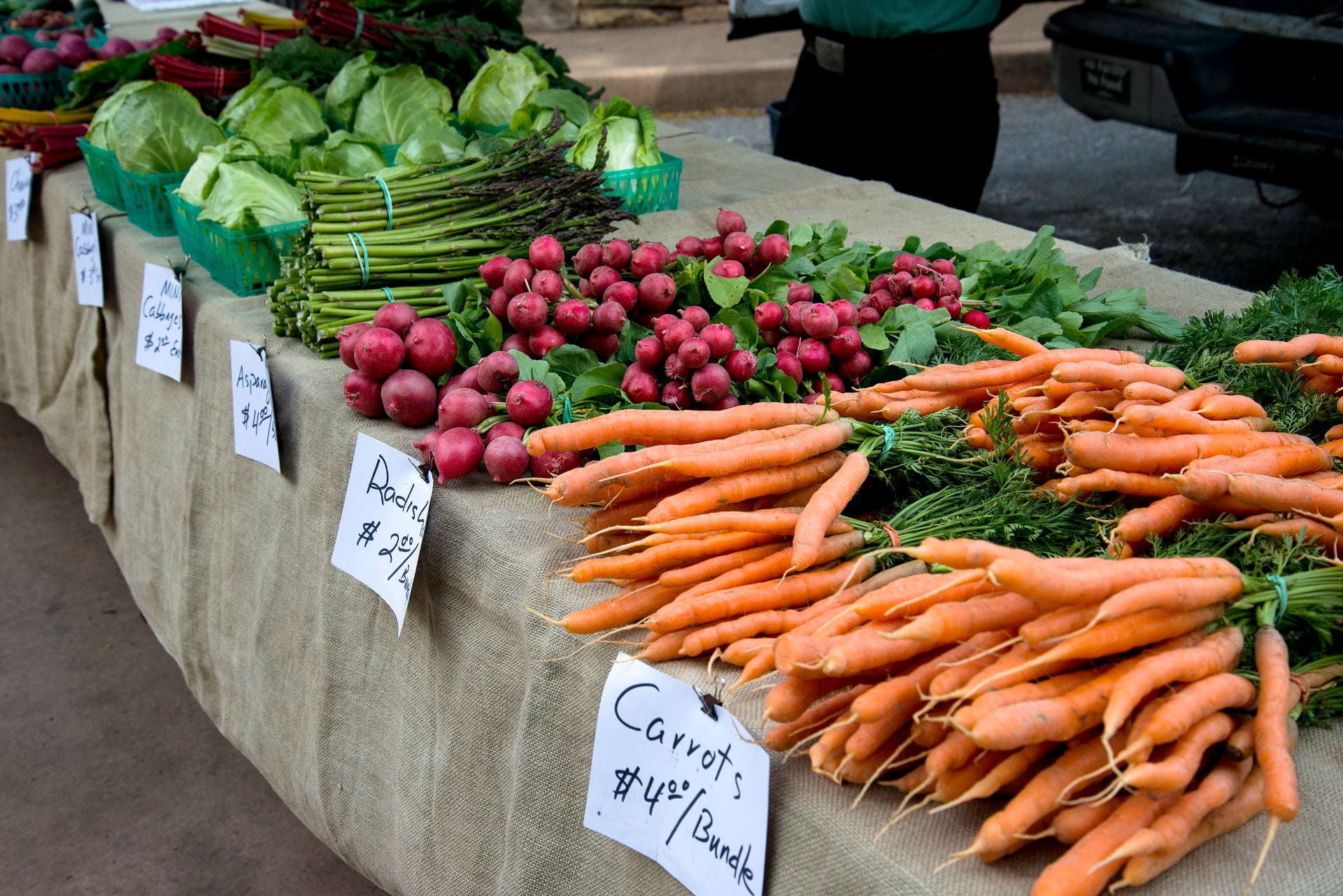 Table at a farmers market, displaying lettuce, asparagus, radishes and carrots for sale.