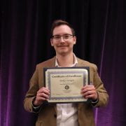 Man poses for camera holding certificate