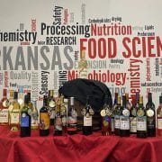 Photo of about 30 wine bottles with gold and silver medals placed on a red tablecloth in front of a word cloud poster with food science terms on it.