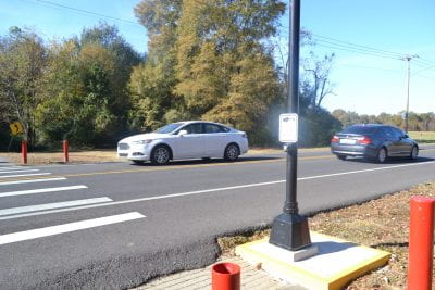 Cars drive past the trailhead with a crosswalk adjacent to the trailhead