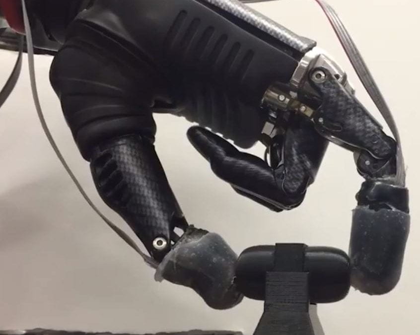 A sleek black prosthetic hand whirs and clicks as the fingers touch a rectangular object, then an egg-shaped one. When a sharply pointed object appears, the bionic hand taps it and recoils, just as a human hand would.