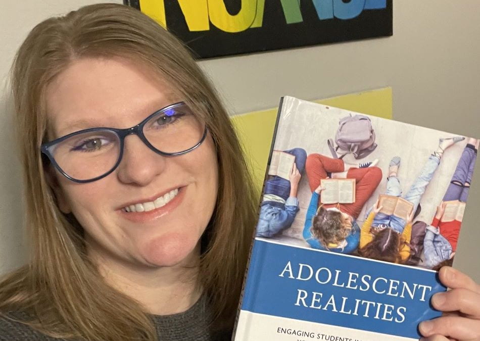 Doctoral student Holly Riesco, holding her book, Adolescent Realities: Engaging Students in SEL through Young Adult Literature.