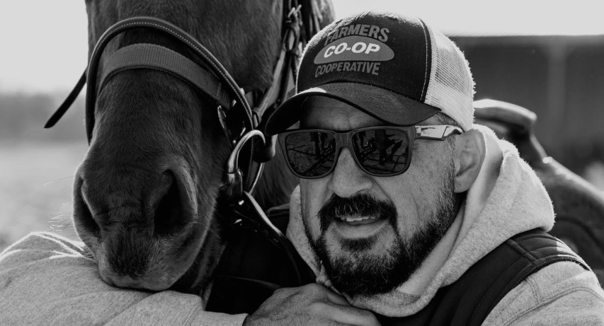 A black and white image of Jared Phillips next to a horse.
