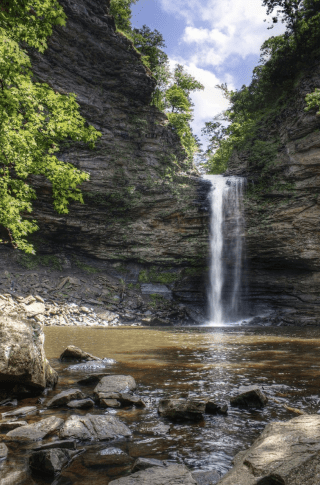 Cedar Falls at Petit Jean State Park; a stream that becomes a narrow waterfall over a small bluff and into a shallow pool. 