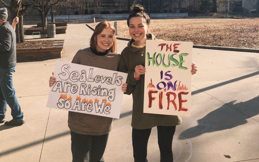Two OMNI members hold signs at a protest in the Union Mall on a winter day. The signs read "Sea levels are rising, so are we" and "the house is on fire."