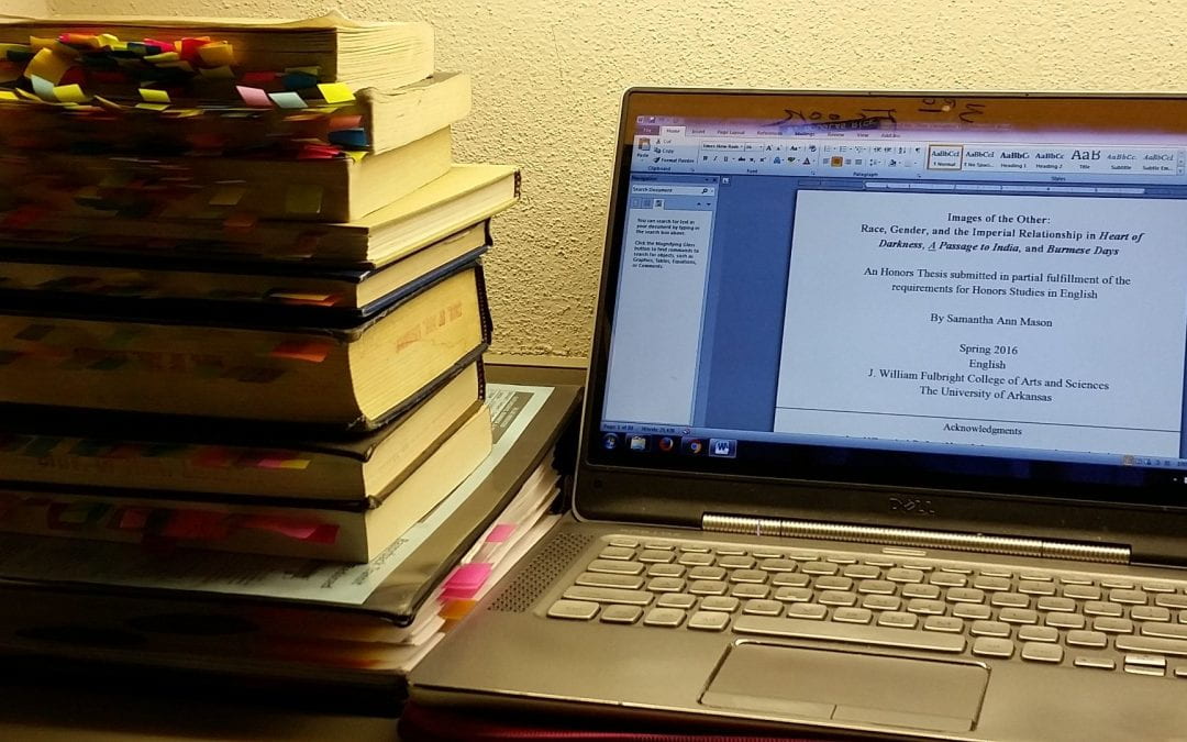 Stack of reference books next to an open laptop with draft of thesis on it.