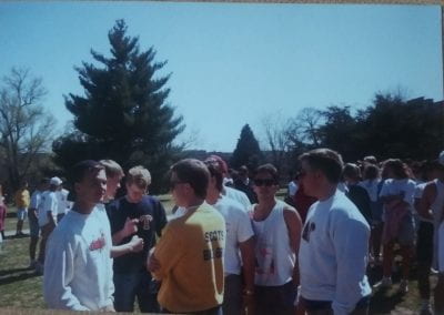 Delta Upsilon 1989 Greek Week outdoors on a sunny day with large crowd of people standing around talking with each other informally.