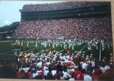 October 15, 1985 U of A versus Texas pregame. A large stadium crowded with people in red and white and red and orange clothing. Many band members are congregating on the field in a performance.